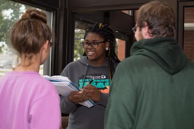 A student with a notebook speaking to two other students